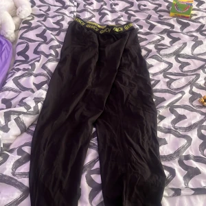 Svarta mjukisbyxor med Grinch-tryck i midjan från H&M - Svarta mjukisbyxor från H&M med elastisk midja där det står 'Grinch' i gult. Perfekta för att chilla hemma eller mysa runt i. Mjukt material och bekväm passform.storlek 146-152