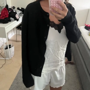 Svart stickad kofta - Mysig svart stickad kofta med knappar framtill. Klassisk modell med lång ärm och rund halsringning. Perfekt att slänga över en topp eller klänning för en enkel och stilren look.