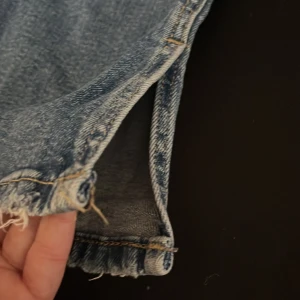  jeans med slits - Säljer ett par klassiska blå jeans med råa fransar nertill. Jeansen har normal passform o slits nertil.