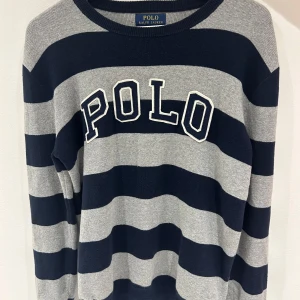 Randig tröja från Polo Ralph Lauren - Säljer en snygg randig tröja från Polo Ralph Lauren i mörkblått och grått. Tröjan har stora blockränder och texten POLO broderad framtill. Perfekt för dig som gillar klassisk stil med en sportig touch.