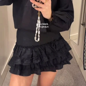 Svart volangkjol från H&M - Supersöt svart kortkjol med flera lager volanger. Kjolen har en bred, smockad midja som ger en bekväm passform och extra volym i kjolen. Perfekt för dig som gillar en lekfull och trendig stil.