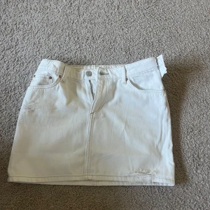 Vit jeanskjol från H&M - Säljer en vit jeanskjol från H&M i klassisk femficksmodell. Kjolen är kort och har en snygg sliten detalj framtill. Perfekt för dig som gillar en enkel men trendig look. Stängs med dragkedja och knapp. Säljer för att den tyvärr var lite för liten men annars superfin och bra