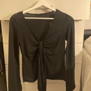 Svart långärmad topp med knyt framtill - Säljer en svart långärmad topp med djup v-ringning och knyt framtill. Toppen har en smickrande passform och är perfekt att styla till olika outfits. Materialet känns mjukt och stretchigt. Lappen är avklippt men skulle gissa storlek S. Kom privat för mått eller bilder 🤗
