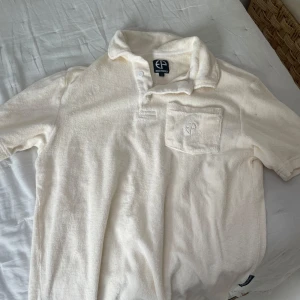 Vit pikétröja från Emilio pendenza - Säljer en vit pikétröja från Epelio e Friends i frotté-material. Tröjan har korta ärmar, klassisk krage och en bröstficka med broderad logga. Perfekt för en avslappnad och stilren look.