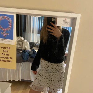 Vit volangkjol med svarta prickar - Säljer en söt vit kjol med svarta prickar och volangdetaljer. Perfekt att styla med en stickad tröja eller en enkel topp.