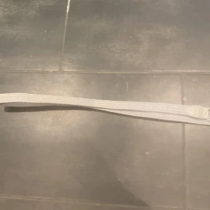 Ljust grått flätat bälte med silverfärgat spänne - Snyggt ljust grått bälte med flätad design och silverfärgat metallspänne. Bältet har detaljer i skinnimitation vid spännet och är flexibelt i materialet. Perfekt för att ge en stilren touch till din outfit.