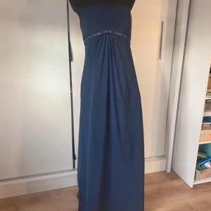 Marinblå axelbandslös långklänning med broderad midja - Säljer en marinblå axelbandslös långklänning med vackert broderad detalj under bysten. Klänningen har ett elegant fall och är perfekt för festligare tillfällen. Dragkedja bak för enkel påklädning.