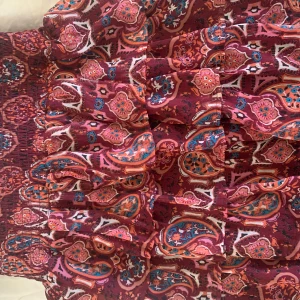 Mönstrad kortkjol i vinröda toner - Säljer en kortkjol med volang och smock i midjan. Kjolen har ett färgstarkt paisleymönster i vinrött, rosa, blått och orange. Perfekt för dig som gillar boho-stil och vill ha något färgglatt i garderoben.