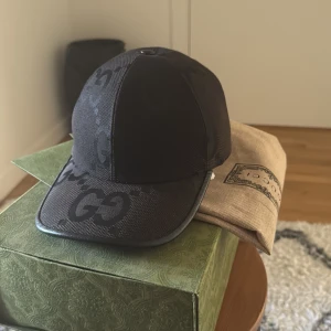 Svart keps med monogram - Snygg svart keps från Gucci med diskret monogrammönster. Kepsen har en justerbar rem baktill för perfekt passform. Perfekt för att ge din outfit en lyxig touch. Perfekt nu för vår/ sommar, priset går att diskuteras hör av er !