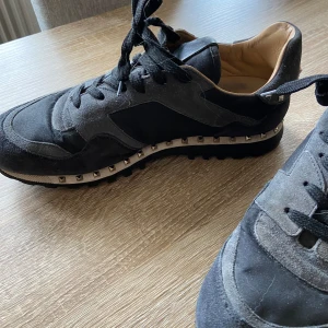 Valentino sneakers med nitar, strl 43 - Snygga grå/svarta sneakers från Valentino med coola nitar runt sulan. Skorna har en kombination av mocka och skinn.  De har snörning och en bekväm passform.