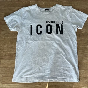 Vit t-shirt från Dsquared2 - Säljer en vit t-shirt från Dsquared2 med texten 'ICON' tryckt i svart på framsidan. T-shirten har en klassisk rund hals och korta ärmar. Blev för liten i tvätten så därför säljer jag den är egentligen 2xl men fittar nu L