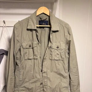 Olivgrön jacka från Morris - Snygg olivgrön jacka från Morris med knappar och två bröstfickor. Jackan har en klassisk krage och är perfekt för en stilren look. Endast använd 2 gånger då den är för liten för mig.                  Nypris :1600kr.                                                        Mitt pris: 500kr
