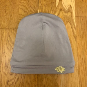 SynaWorld mössa - Snygg grå mössa med en diskret broderad logga i gult. Perfekt för kyliga dagar och enkel att matcha med olika outfits.