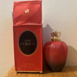 Pink Poison Eau de Parfum - Elegant parfymflaska i röd nyans med en guldtonad spraypump. Flaskan har en rundad form och kommer med en matchande röd förpackning. Doften är en del av Story of Love-kollektionen och innehåller 100 ml av Eau de Parfum.