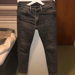 Grå jeans från Levi's - Snygga svart och grå jeans från Levi's med en klassisk femficksdesign. De har en slim passform och är tillverkade i ett slitstarkt denimtyg. Perfekta för en stilren look.Levi’s 519 är en smal passform. Ny pris 699 mit pris 250. kontakta mig om du har några frågor. W30 L32