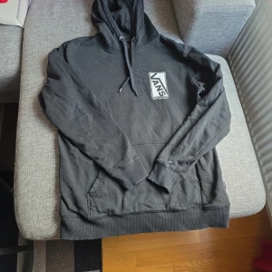 Svart hoodie från Vans - Säljer en svart hoodie från Vans med stor logga och texten 'Off The Wall' på ryggen. Tröjan har en klassisk känguruficka och justerbar huva med dragsko. Perfekt för en avslappnad stil.