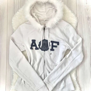 Vit hoodie med pälsdetaljer från Abercrombie & Fitch - Jätte fin zip up tröja från ambercrombie & fitch. Den är köpt på vinted för ett tag sen. Om man kollar på bilderna så ser man att själva pälsen runt om den sitter lite löst(den har inte ramlat av) jag har suttit säkerhetsnålar på vissa ställen. (Hon jag köpte tröjan av har sytt på pälsen själv) inte äkta päls