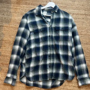 Svartvit rutig skjorta - En Snygg, väldigt eftertraktad Grön-Blåvittrutig skjorta med långa ärmar och knappar framtill. Skjortan har två bröstfickor med lock och en klassisk krage. Perfekt för en avslappnad stil.