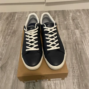 Svarta sneakers från Paul Smith - Splitternya snygga marinblå sneakers från Paul Smith med vita detaljer och färgglada ränder på hälen. Skorna har vita snören och en vit sula. Perfekta för en stilren look. Säljer dessa skor eftersom jag köpte dom i fel storlek. Pris kan diskuteras i dm.