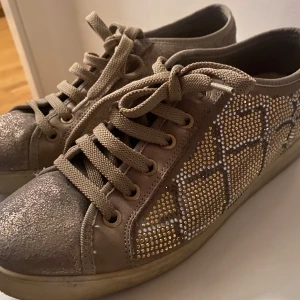 Beige sneakers med glittriga detaljer - Snygga beige sneakers med glittriga detaljer!!💕. Skorna har ett mönster av små pärlor på sidorna som ger en extra touch av glamour. Köpta second hand, själv har jag använt dem få gånger! Pris kan diskuteras! 