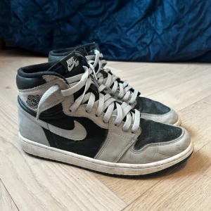 Nike Air Jordan 1 Retro High Shadow 2.0 - Säljer ett par klassiska Nike Air Jordan 1 Retro High OG i svart och grått. Skorna har en ikonisk design med snörning och Nike-logga på sidan. Perfekta för sneakerheads som älskar en tidlös stil. Jag betalade 500€