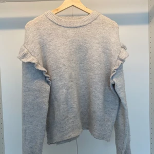 Stickad tröja med volanger - Stickad tröja som är grå med volanger. Är superfin och använd. Men det är inte nödvändigt synligt. Är i storlek 164 men är stor i storleken och passar S mer. 