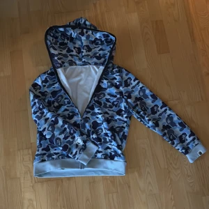 Bape hoodie - Säljer en blå camo hoodie från Bape. Skick 10/10 nästan helt ny men inga tecken på användning. Storlek S men passar M.  OBS!! Pris kan diskuteras.