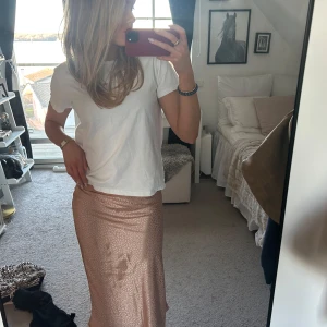 Glansig långkjol  - Säljer en glansig långkjol i en vacker champagne nyans. Kjolen har en elegant passform och är perfekt för att lysa upp vilken outfit som helst. Den är tillverkad i ett skimrande material som fångar ljuset fint.