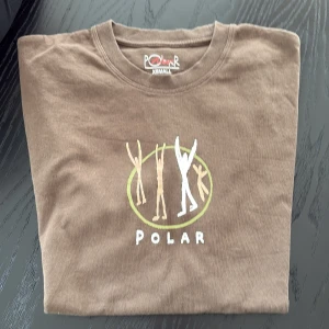 Brun t-shirt från Polar Skate Co. - Säljer en brun t-shirt från Polar Skate Co. med ett coolt tryck på framsidan. T-shirten är kortärmad och gjord i mjuk bomull. Perfekt för en avslappnad stil.