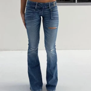 Pleated flare jeans Gina  - Snygga blå bootcut jeans med slitningar på låren och knäna. Låg midjade från Gina i strl S helt oanvända med lapp på men kan ej lämna tillbaks.
