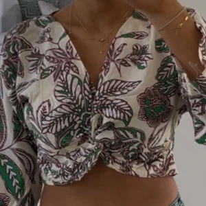 Mönstrad omlottopp - Snygg mönstrad omlottopp med gröna och lila bladmotiv. Toppen har en knytdetalj framtill och långa ärmar. Perfekt för en trendig look!