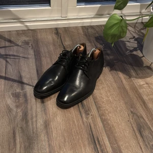 (Nyskick) Clarks svarta skinnskor, skoblock ingår. - Snygga svarta skinnskor från Clarks med klassisk snörning. Perfekta för en stilren look. Skorna har en robust sula och en elegant design som passar till många tillfällen. Använda en gång, har aldrig fått tid att använda dem. Använda en gång på ett fest evenemang.