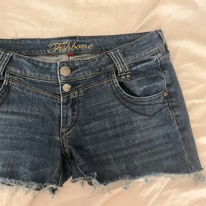 Jeansshorts från Fishbone - Snygga jeansshorts från Fishbone med fransiga kanter och dubbla knappar fram. De har en cool dragkedjedetalj på bakfickan och klassiska femficksdesign.💕💕