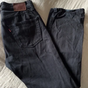Svarta jeans från Levis - Säljer ett par klassiska svarta jeans från Levis. De har en normal passform och är perfekta för en stilren look. Jeansen har en bakficka med en liten röd etikett och en läderpatch vid midjan.