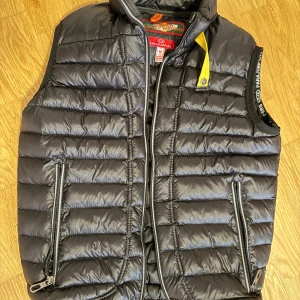 Svart väst från Parajumpers. Kör bara utbyten priset gäller ej - Säljer en svart dunväst från Parajumpers med dragkedja och gul detalj vid kragen. Västen har en quiltad design och är superlätt, perfekt för lager-på-lager. Märkesdetaljer finns på insidan och utsidan. Bara utbyten priset gäller ej!