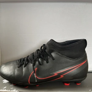 Helt nya Nike Mercurial fotbollsskor storlek 37 - Säljer ett par helt nya och oanvända Nike Mercurial fotbollsskor i storlek 37. Perfekta för spel på gräs, ger bra grepp och komfort. 	•	Märke: Nike 	•	Modell: Mercurial (osäker på exakt modell) 	•	Färg: Svart med röda detaljer 	•	Skick: Helt nya, aldrig använda 	•	Storlek: 37  Finns att hämta i Hässleholm . Kan skickas mot fraktkostnad.  Pris: 700 kr (kan diskuteras vid snabb affär)  Skicka PM om du är intresserad!