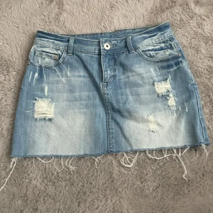 Lågmidjad jeanskjol från vila - Ljusblå jeanskjol från Vila i kort modell med slitna detaljer och fransig nederkant. Perfekt för en avslappnad och trendig look. Priset är ej hugget i sten. Storlek M men passar även S