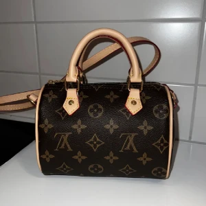 monogram handväska - Snygg handväska i klassiskt monogrammönster. Väskan är brun med beige detaljer och har både handtag och axelrem. Guldiga metalldetaljer och dragkedja. Perfekt storlek för det viktigaste och en riktig statement piece.