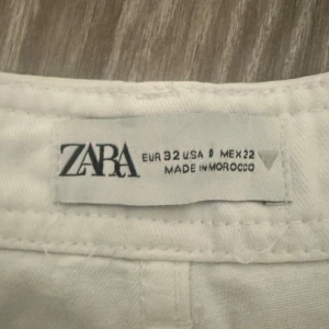 Vita cargobyxor från Zara - Säljer ett par vita cargobyxor från Zara i storlek 32. Byxorna har flera praktiska fickor på sidorna och raka ben. Perfekta för en chill och trendig look. Materialet känns som bomull och de har klassisk cargostil med knapp och dragkedja i midjan.