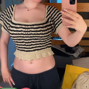 Randig croppad stickad topp - Superfin croppad stickad topp med svart och beigea ränder. Toppen har korta ärmar, fyrkantig urringning och en söt volangkant nertill. Perfekt för dig som gillar en trendig och unik look!