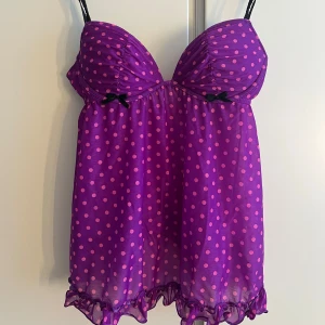 Babydoll topp - Supersöt lila babydoll topp med rosa polkadots från La Senza. Tunna axelband och volangkant nertill. Toppen har lätt vadderade kupor och små svarta rosetter framtill. Säljer pga att kuporna är lite för små💔tror det är en B kupa. Materialet är genomskinligt (inte på kuporna dock) Priset kan diskuteras🫶