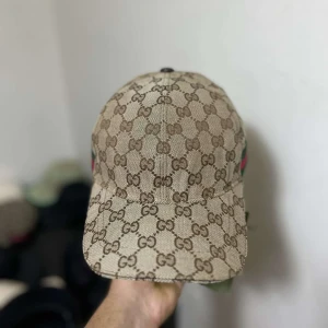 Beige keps från Gucci - Säljer en snygg beige keps från Gucci med deras ikoniska GG-mönster. Kepsen är i mycket bra skick och har justerbart band för perfekt passform. Fick kepsen som present men vill inte ha den använd 6-7 gånger. Boxen finns och dustbag!🧢                                           Priset kan diskuteras.