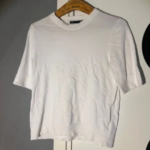 Vit stickad kortärmad tröja 157 - Enkel och stilren vit stickad tröja från 157 med korta ärmar och rund halsringning. Tröjan har ribbade muddar vid ärmslut och nederkant, vilket ger en clean och fräsch look. Perfekt att matcha med jeans eller kjol för en chill vibe.