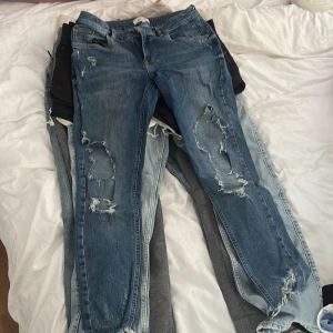 Blå slitna jeans med hål - Ett par blå jeans med slitningar och hål på knäna och låren. Jeansen har klassisk femficksmodell och normal passform. Storleken på jeansen är 12. Köpta för 700
