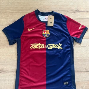 FC Barcelona Lamine Yamal tröja Nike M - Snygg FC Barcelona matchtröja från Nike med Lamine Yamal och nummer 19 på ryggen. Tröjan är blå och röd med gul Nike-logga, klubbmärke och Cactus Jack-tryck framtill. Tillverkad i lätt och ventilerande material, perfekt för fotbollsälskare.