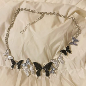 Silverfärgat halsband med fjärilar - Unikt halsband med stora och små fjärilar i silver och svart. Kedjan är grovlänkad och justerbar. Fjärilarna har detaljerade vingar och ger ett coolt statement till din outfit. Perfekt för dig som vill sticka ut med accessoarer som känns trendiga och lekfulla.