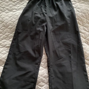 Svarta wide byxor från H&M - Svarta byxor från H&M i storlek 158. De har en bred, elastisk midja med rynk och vida ben för en chill och trendig look. Perfekta att styla med en crop top eller hoodie. Materialet känns lätt och skönt mot huden.