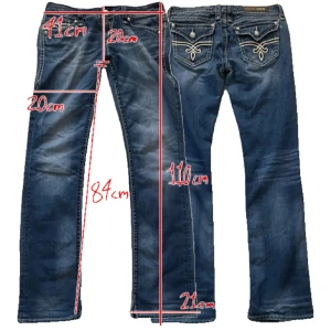 Rock Revival Kristen Straight jeans - Snygga blå jeans från Rock Revival, modell Kristen Straight. Klassisk femficksdesign med vita broderade detaljer och dekorativa bakfickor. Jeansen har raka ben och orange kontrastsömmar. Perfekta för dig som gillar en cool och unik denimstil.