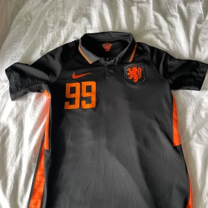 Holländsk Nike fotbollströja  svart/orange - Snygg svart fotbollströja från Nike med orange detaljer, nummer 99 och namnet Vigge på ryggen. KNVB-logga på bröstet och klassisk krage med orange kant. Tillverkad i Dri-FIT-material som andas, perfekt för träning eller match.