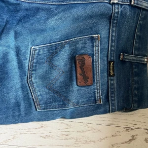 Vintage jeans från Wrangler - Klassiska blå jeans från Wrangler med vida ben och snygga detaljer på bakfickan. Jeansen har normal passform och är tillverkade i slitstarkt denimtyg. Perfekta för dig som gillar en tidlös och avslappnad stil. Köpta på Broadway & Sons
